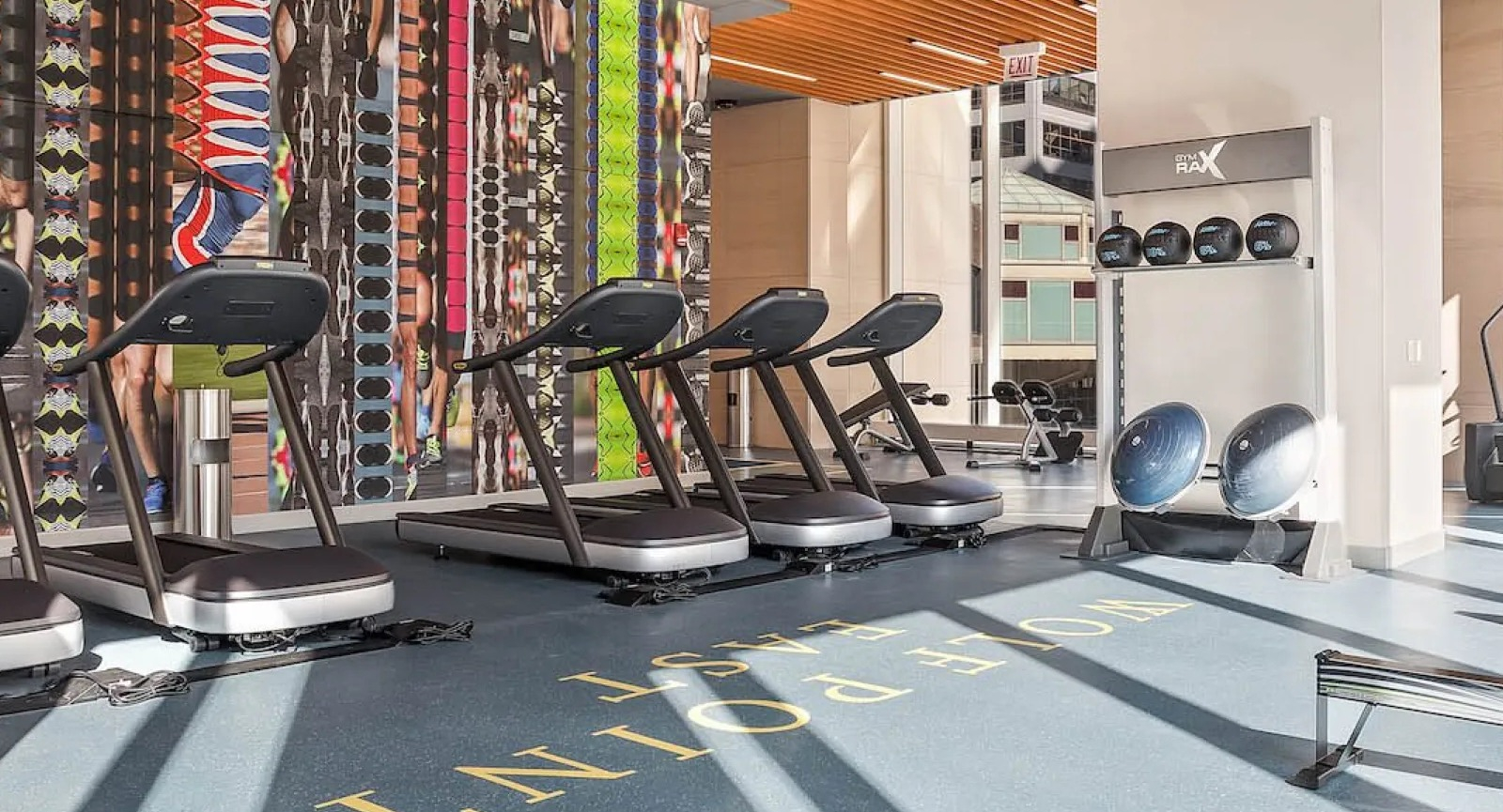 Modern fitness center with treadmills, rowing machines, and colorful wall art at Wolf Point East apartments in Chicago