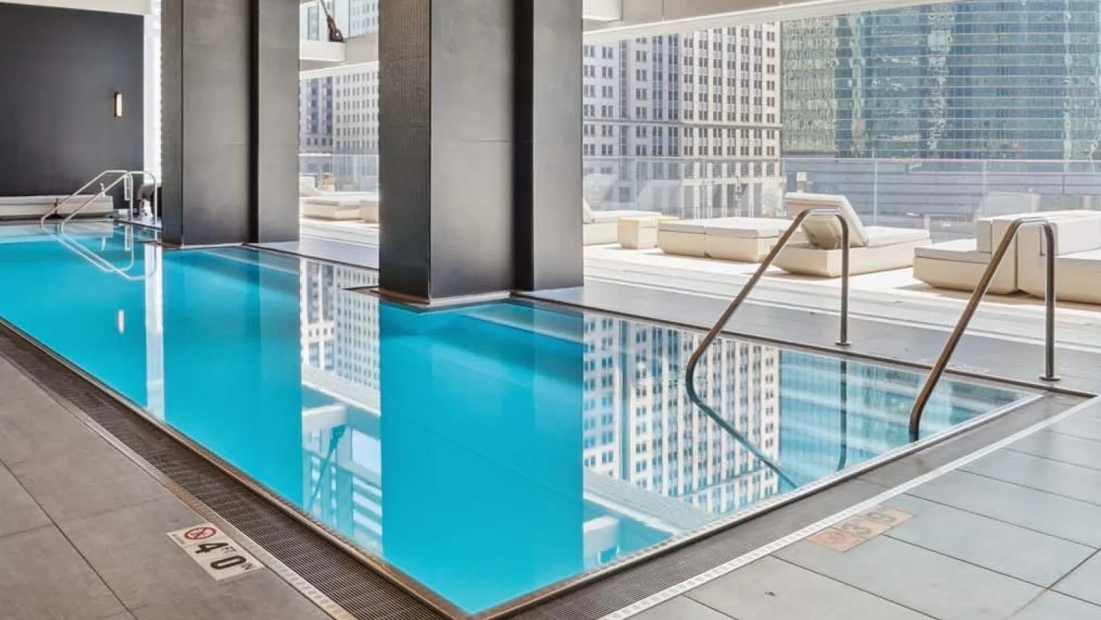 Beautiful indoor lap pool with floor-to-ceiling windows and ample lounge seating at Wolf Point East apartments in Chicago