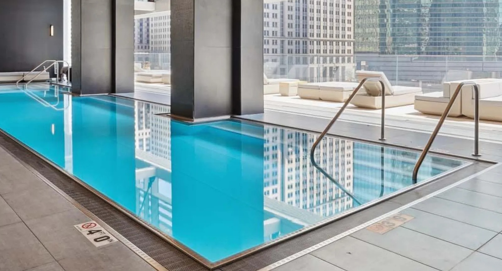 Beautiful indoor lap pool with floor-to-ceiling windows and ample lounge seating at Wolf Point East apartments in Chicago