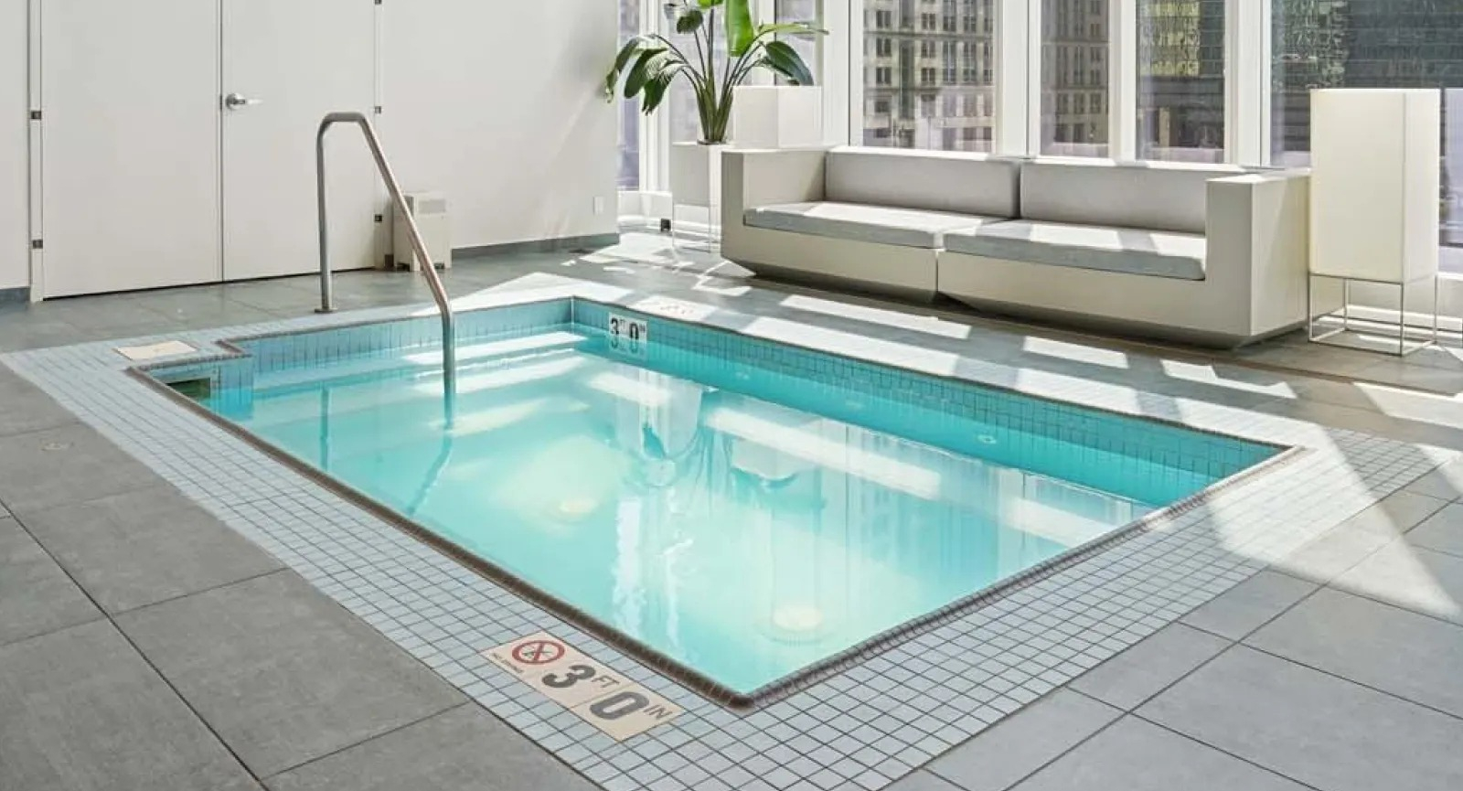 Serene indoor pool area with large windows offering panoramic city views and comfortable seating at Wolf Point East in Chicago