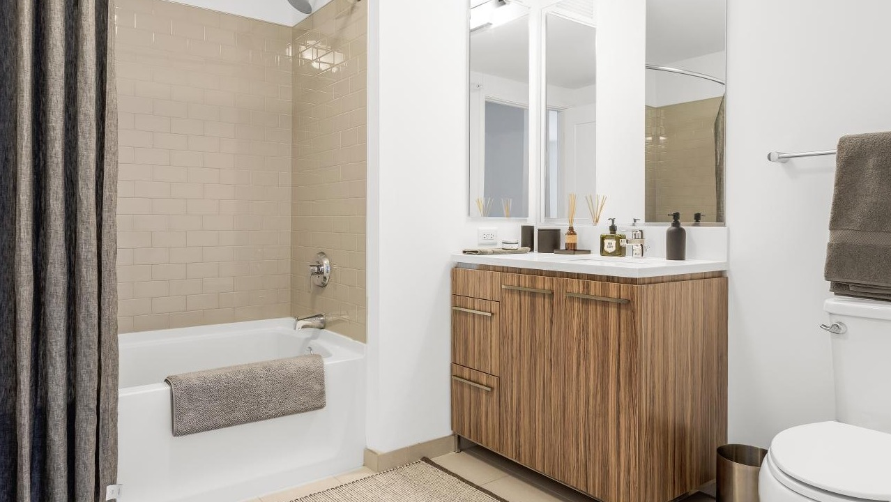 Modern bathroom at Wolf Point West apartments in Chicago with bathtub, wood vanity, and stylish tile walls