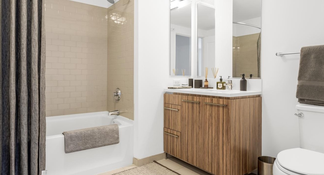 Modern bathroom at Wolf Point West apartments in Chicago with bathtub, wood vanity, and stylish tile walls