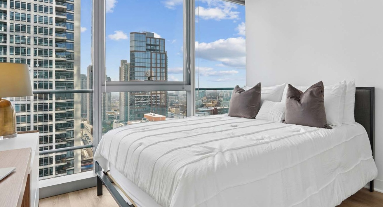 Modern bedroom at Wolf Point West apartments in Chicago with floor-to-ceiling windows and skyline views