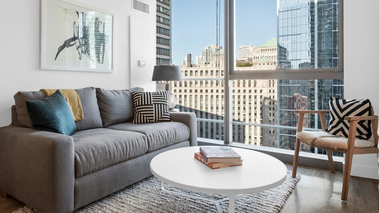 Cozy living nook with gray sofa, round white coffee table, accent chair, and large windows showcasing downtown Chicago at Wolf Point West apartments