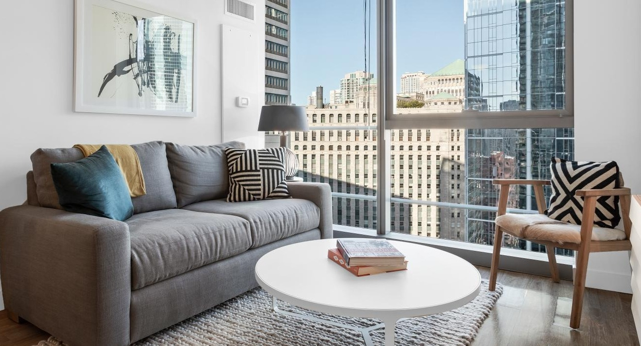 Cozy living nook with gray sofa, round white coffee table, accent chair, and large windows showcasing downtown Chicago at Wolf Point West apartments