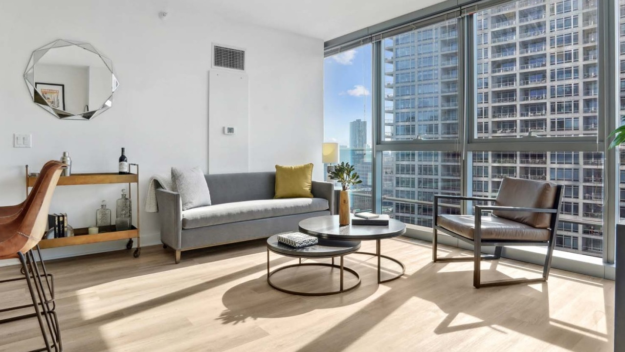 Bright living room at Wolf Point West apartments in Chicago with modern furniture, large windows, and a cozy city view