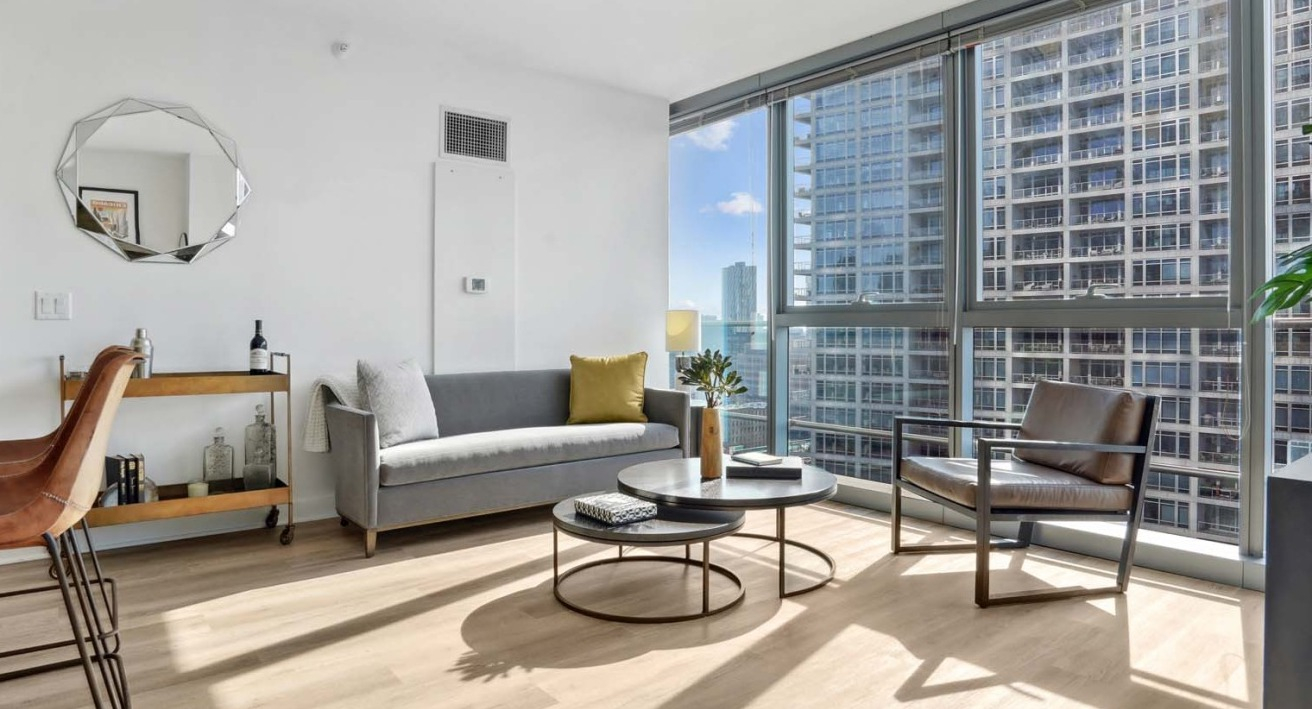 Bright living room at Wolf Point West apartments in Chicago with modern furniture, large windows, and a cozy city view