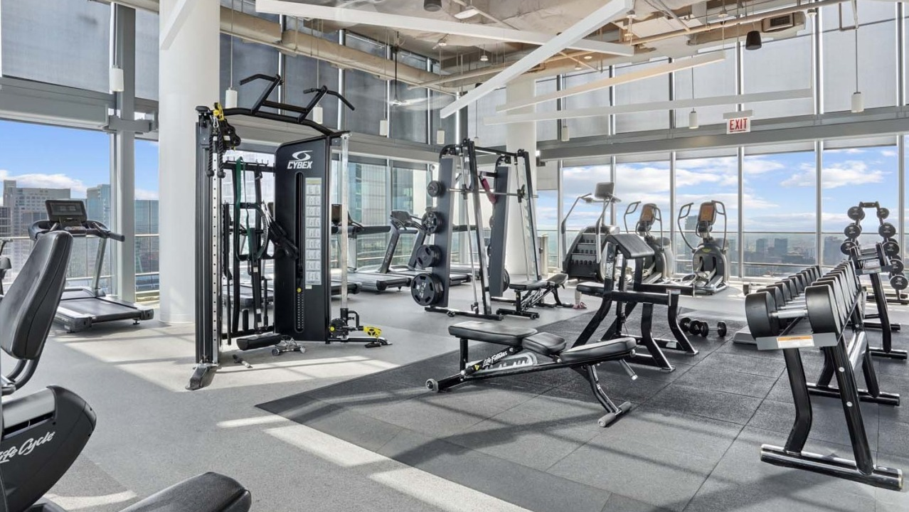 Spacious fitness center at Wolf Point West apartments in Chicago with cardio machines, weights, and city views