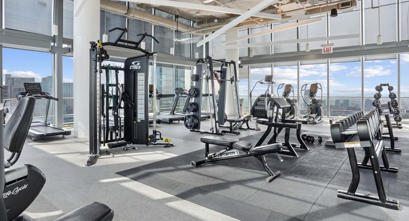 Spacious fitness center at Wolf Point West apartments in Chicago with cardio machines, weights, and city views