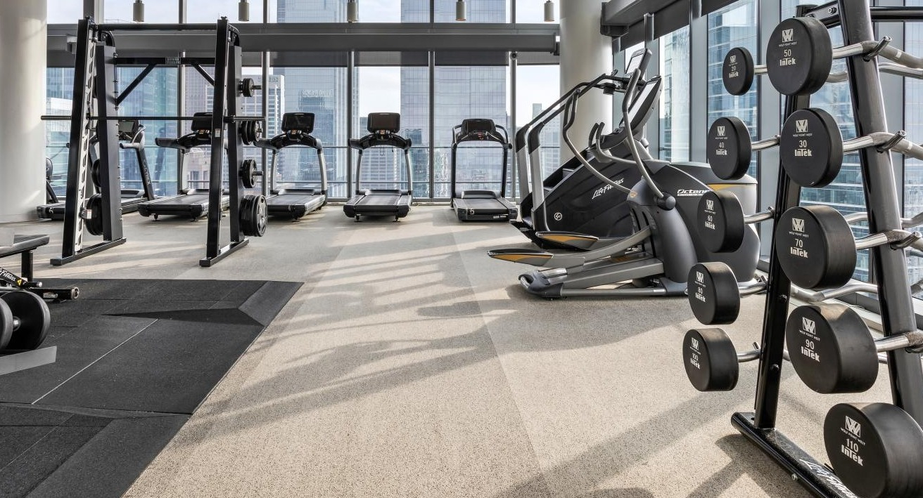 Modern gym at Wolf Point West apartments in Chicago featuring free weights, treadmills, and large windows with skyline views