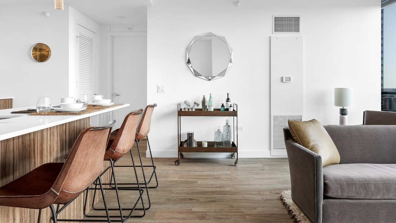 Open kitchen with quartz island and bar seating overlooking a bright living room with city views at Wolf Point West luxury apartments in Chicago