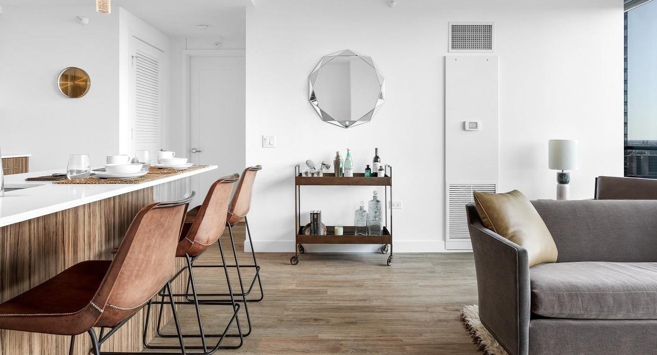 Open kitchen with quartz island and bar seating overlooking a bright living room with city views at Wolf Point West luxury apartments in Chicago