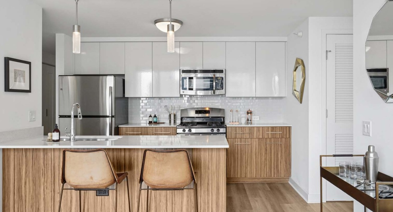 Modern kitchen with stainless steel appliances, glossy white cabinets, wood accents, and a large island with sink at Wolf Point West apartments in Chicago