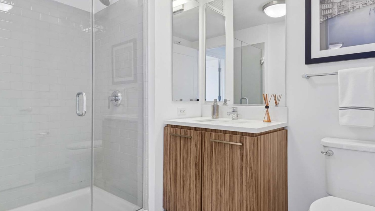 Elegant bathroom at Wolf Point West apartments in Chicago with glass shower, wood vanity, and modern fixtures