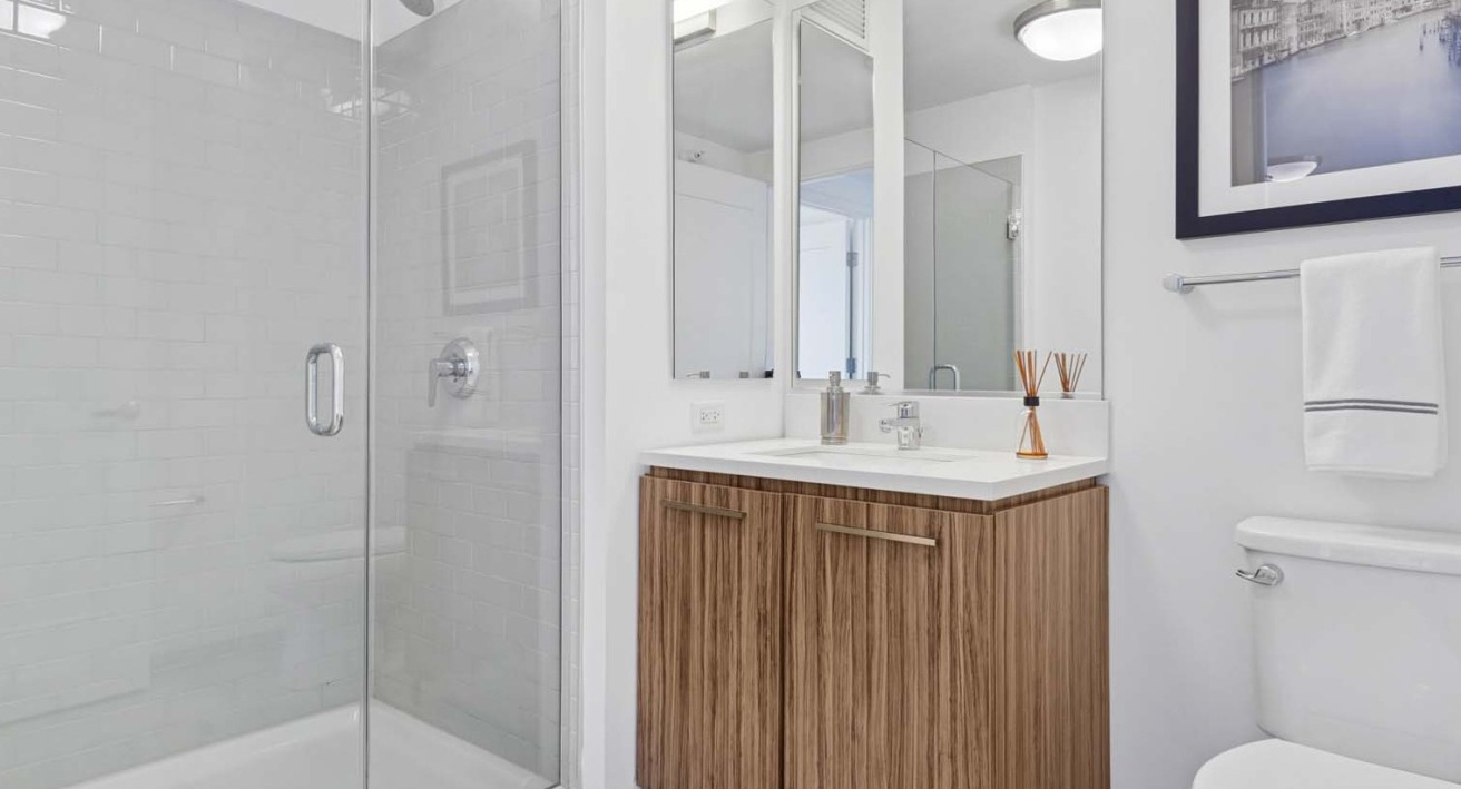 Elegant bathroom at Wolf Point West apartments in Chicago with glass shower, wood vanity, and modern fixtures