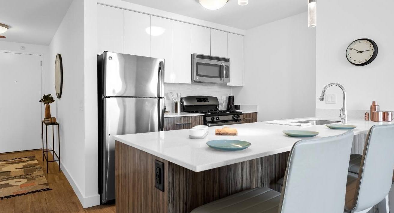 Contemporary kitchen with quartz island breakfast bar, pendant lighting, and stainless appliances near the entry at Wolf Point West apartments in Chicago