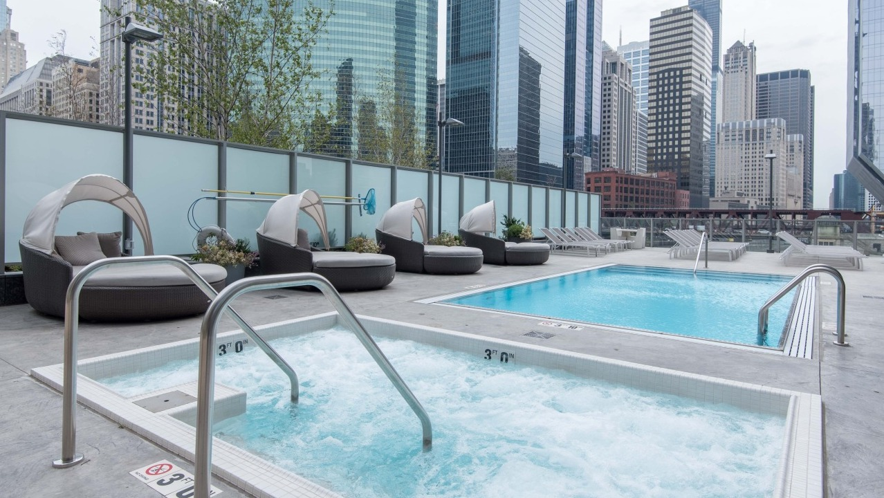 Outdoor pool deck at Wolf Point West apartments in Chicago featuring hot tub, poolside loungers, and skyline views