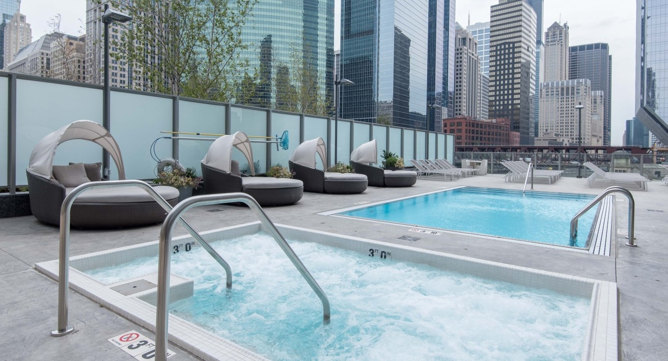 Outdoor pool deck at Wolf Point West apartments in Chicago featuring hot tub, poolside loungers, and skyline views