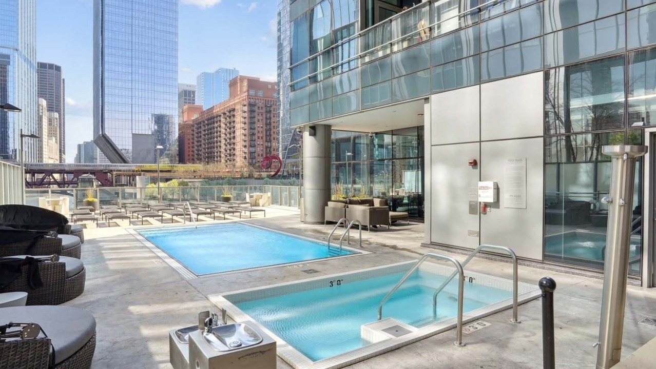 Modern swimming pool at Wolf Point West apartments in Chicago with cabanas, lounge seating, and skyline backdrop