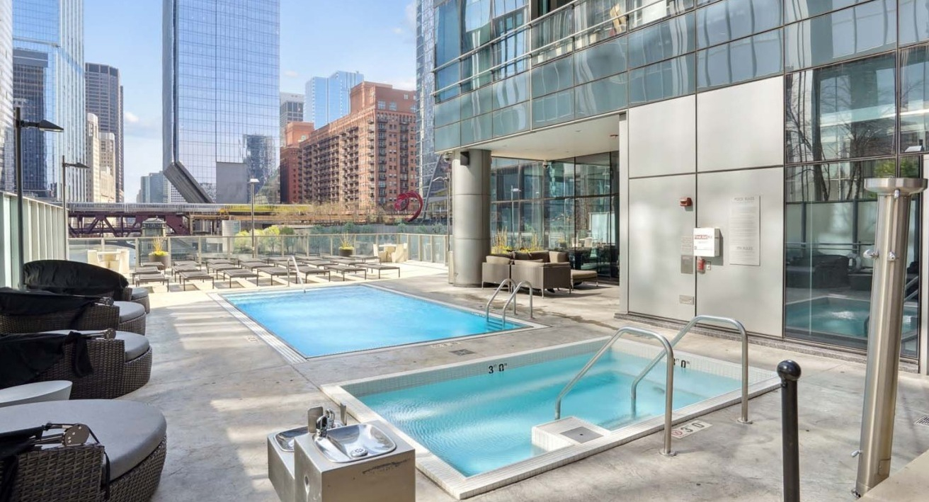 Modern swimming pool at Wolf Point West apartments in Chicago with cabanas, lounge seating, and skyline backdrop