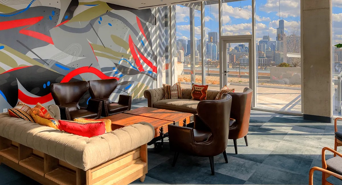 Vibrant resident lounge with abstract wall art, comfortable seating, and large windows offering city views at Xavier Apartments in Chicago