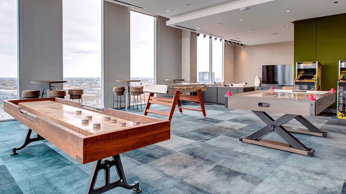 Fun game room with shuffleboard tables, arcade games, and city views from large windows at Xavier Apartments in Chicago