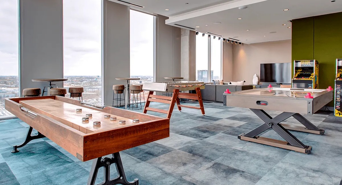 Fun game room with shuffleboard tables, arcade games, and city views from large windows at Xavier Apartments in Chicago