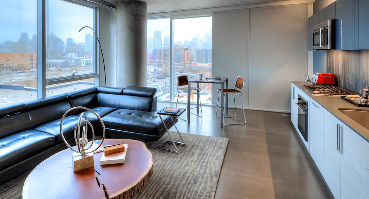Open concept kitchen and living room with modern black sectional, dining area, and city views at Xavier Apartments in Chicago
