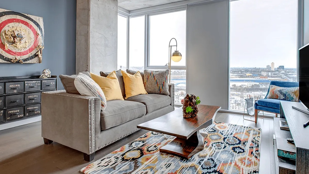 Contemporary living room with a comfortable sofa, colorful rug, and large windows providing a city vista at Xavier Apartments in Chicago