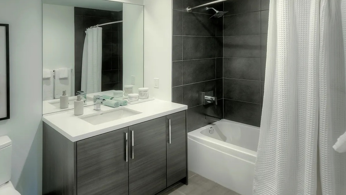 Modern bathroom with a dark wood vanity, white toilet, and a shower-tub combination with sleek black tiles at Xavier Apartments in Chicago