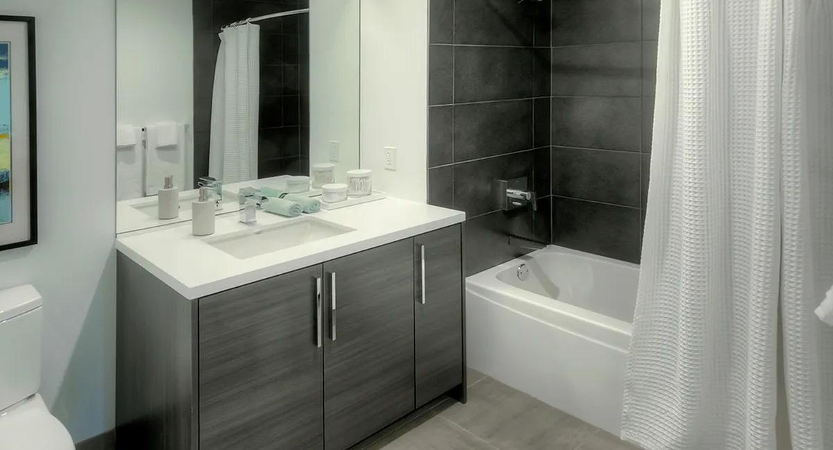 Modern bathroom with a dark wood vanity, white toilet, and a shower-tub combination with sleek black tiles at Xavier Apartments in Chicago