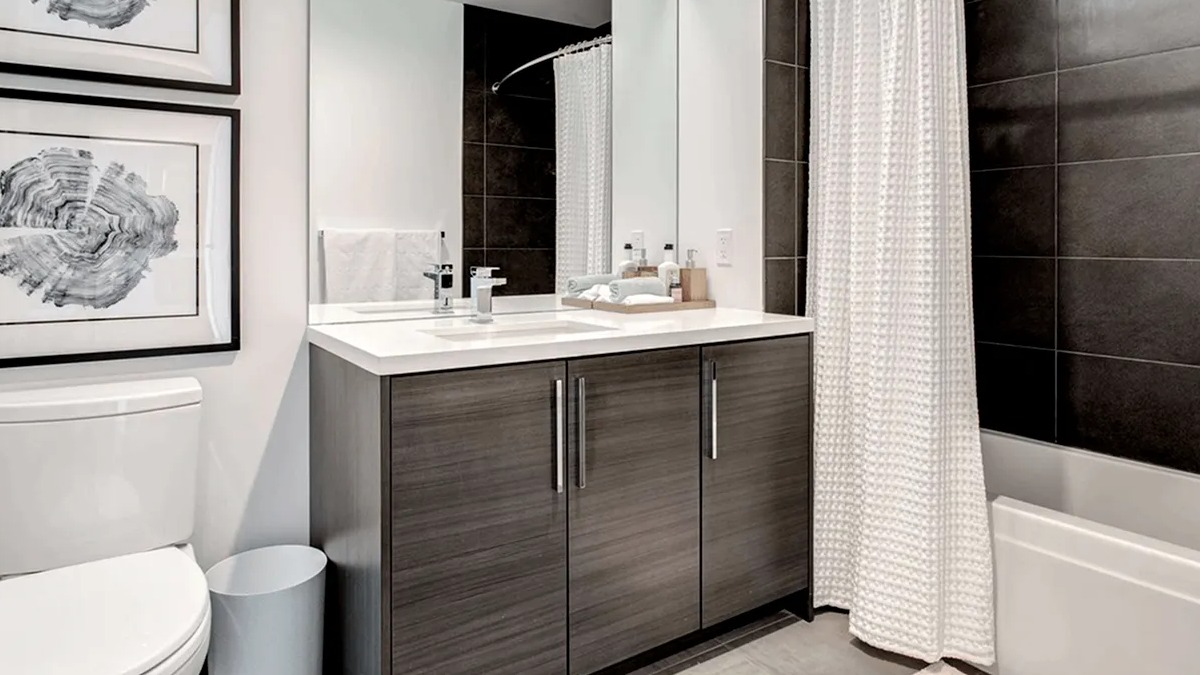 Contemporary bathroom with a dark wood vanity, white toilet, and a shower-tub combination with sleek black tiles at Xavier Apartments in Chicago