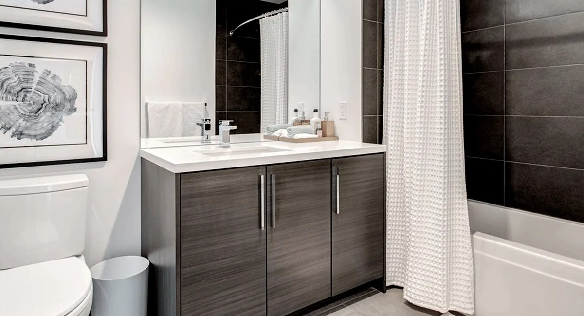 Contemporary bathroom with a dark wood vanity, white toilet, and a shower-tub combination with sleek black tiles at Xavier Apartments in Chicago