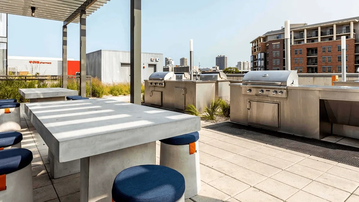 Outdoor grilling station with multiple grills, communal tables, and seating on a sunny terrace at Xavier Apartments in Chicago