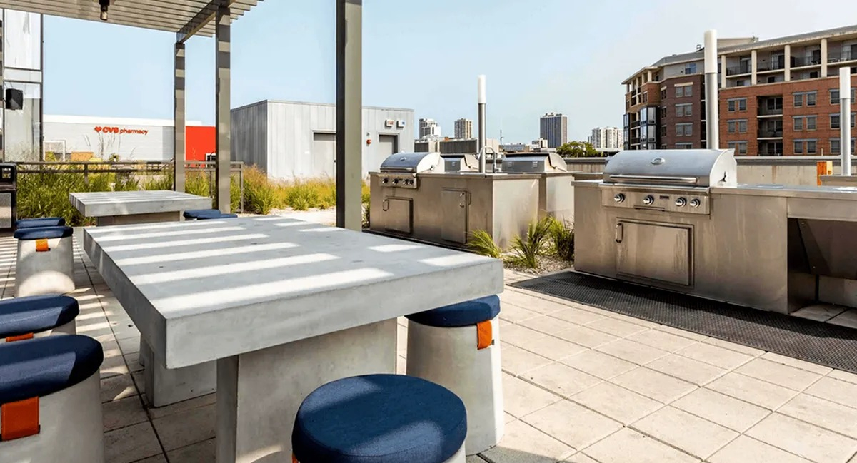 Outdoor grilling station with multiple grills, communal tables, and seating on a sunny terrace at Xavier Apartments in Chicago