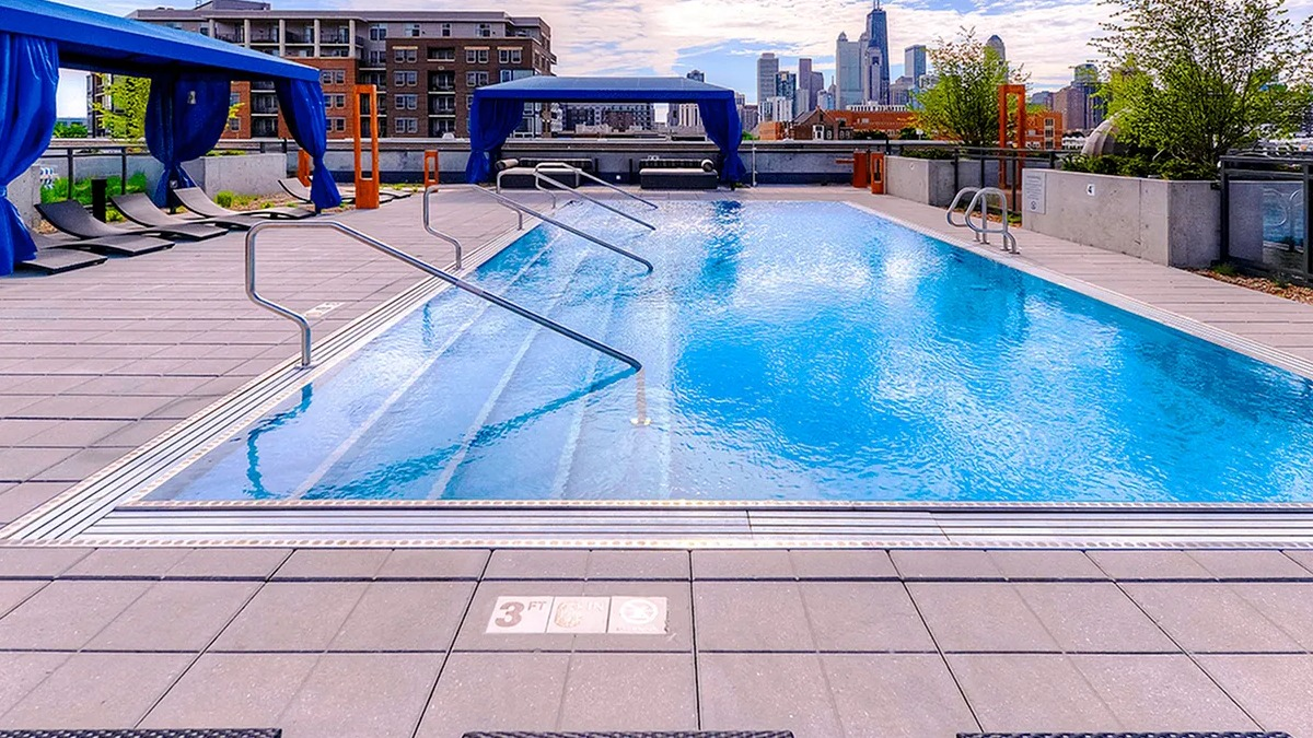 Luxurious outdoor pool area with comfortable lounge chairs under blue canopies and impressive city views at Xavier Apartments in Chicago