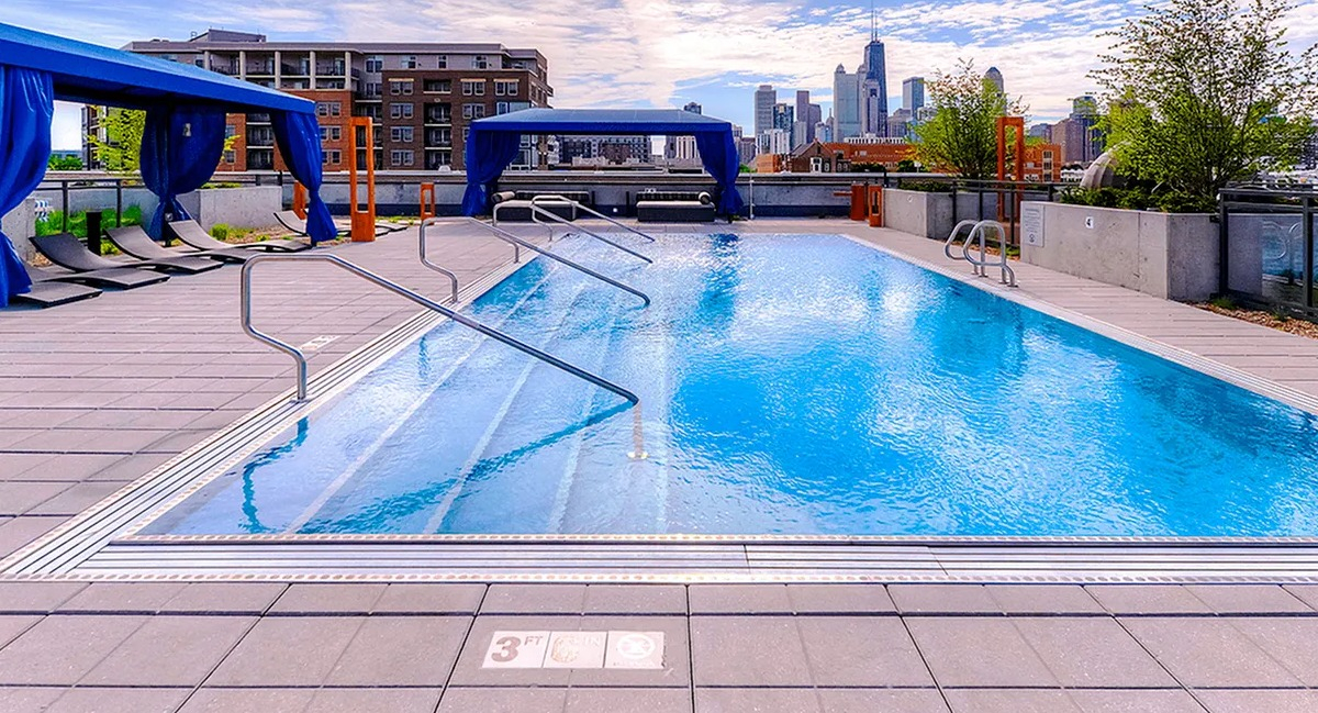 Luxurious outdoor pool area with comfortable lounge chairs under blue canopies and impressive city views at Xavier Apartments in Chicago